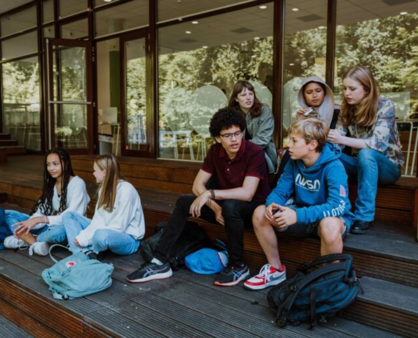 Een groepje jongeren zit op trappen voor de school